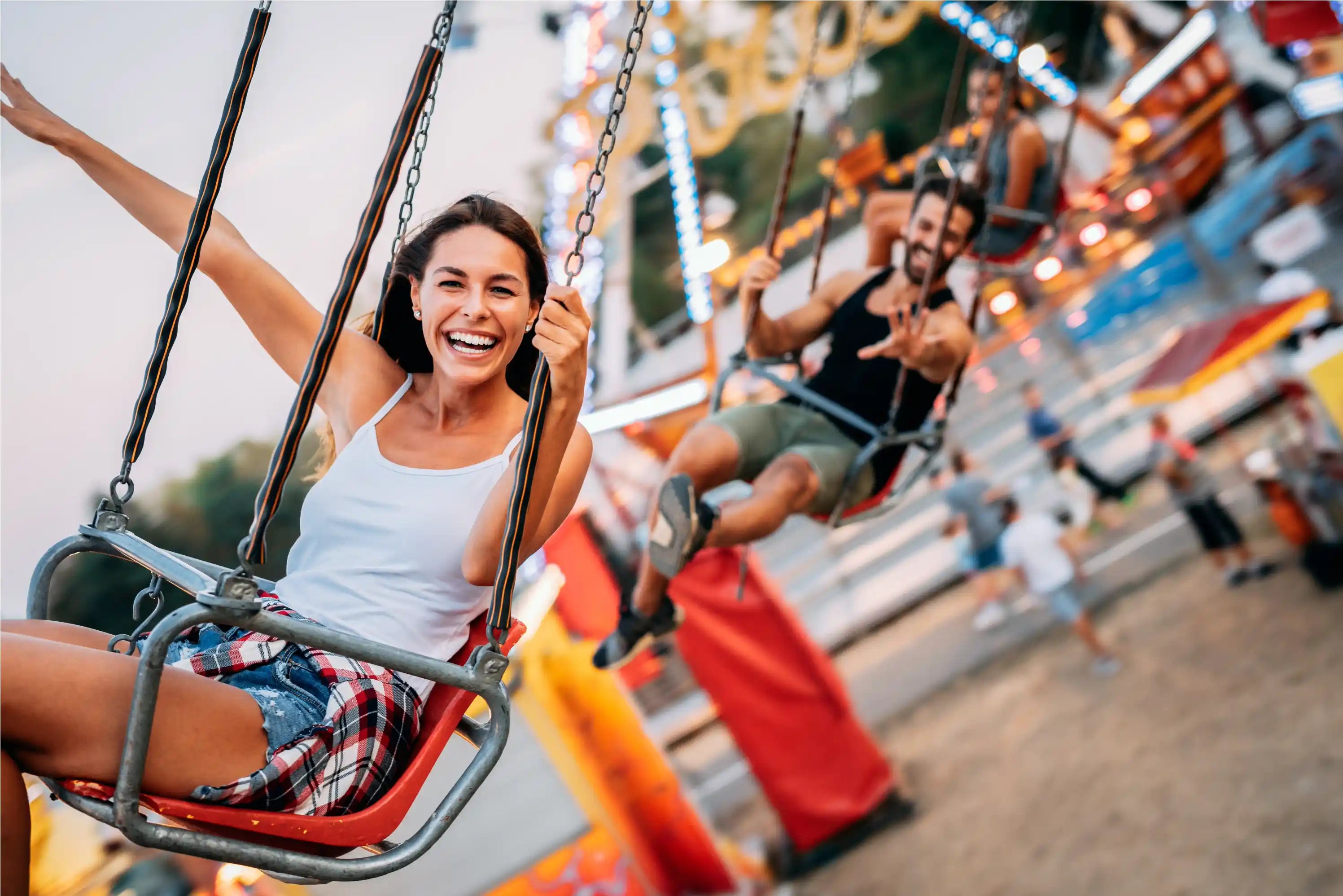 Woman smiling openly as she spins around in a chair hanging from a ride at an amusement park