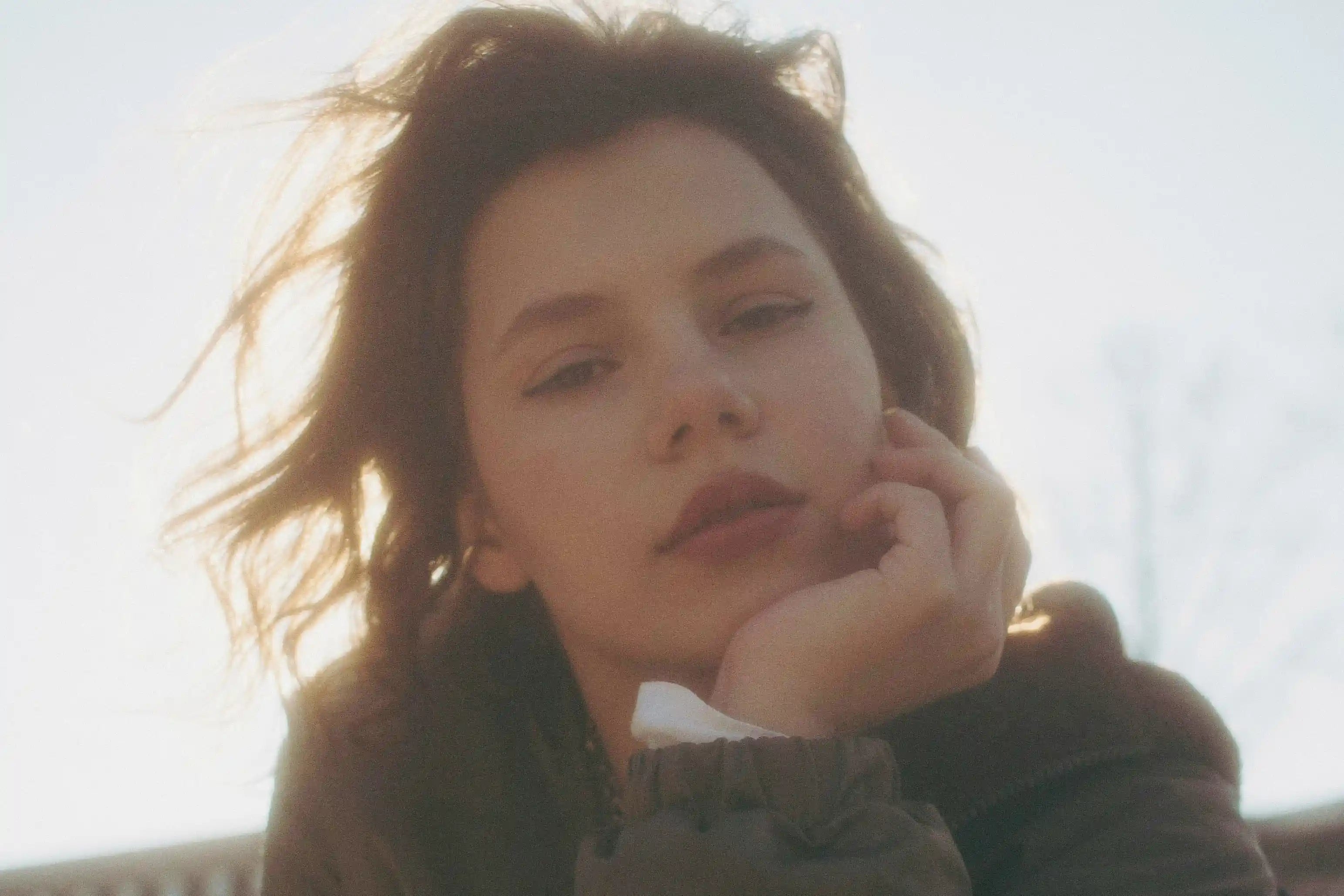 A portrait of a calm young woman outdoors with the sun behind her